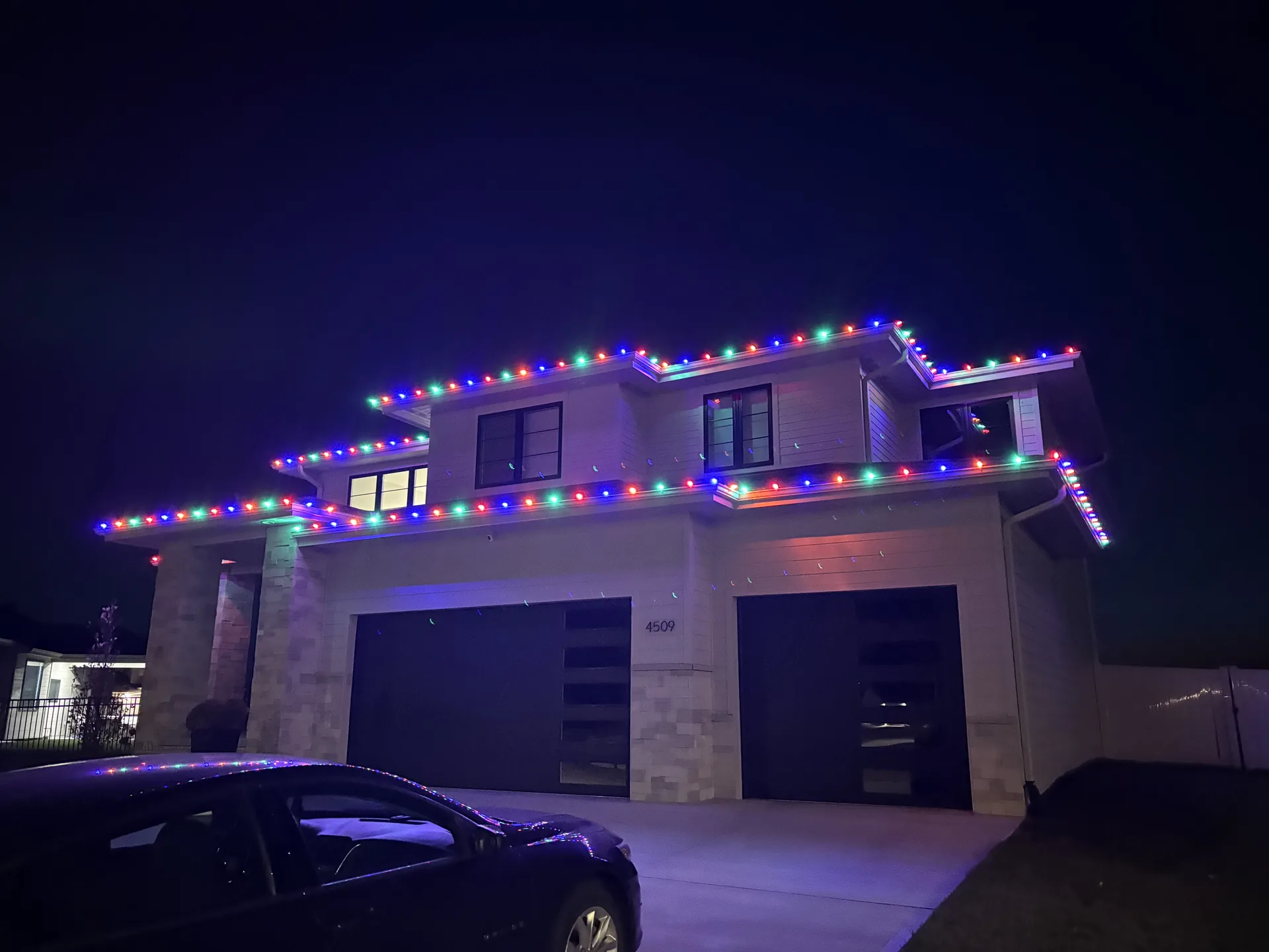 Purple and green holiday lighting across a modern two-story facade