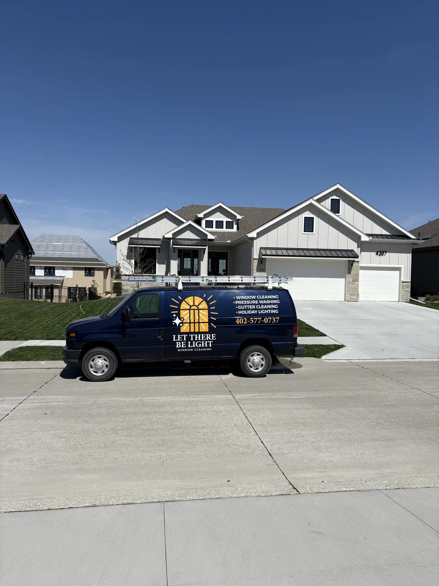 Let There Be Light technician cleaning exterior glass on a brick and siding home in Omaha, Nebraska — with tracks and sills detailed